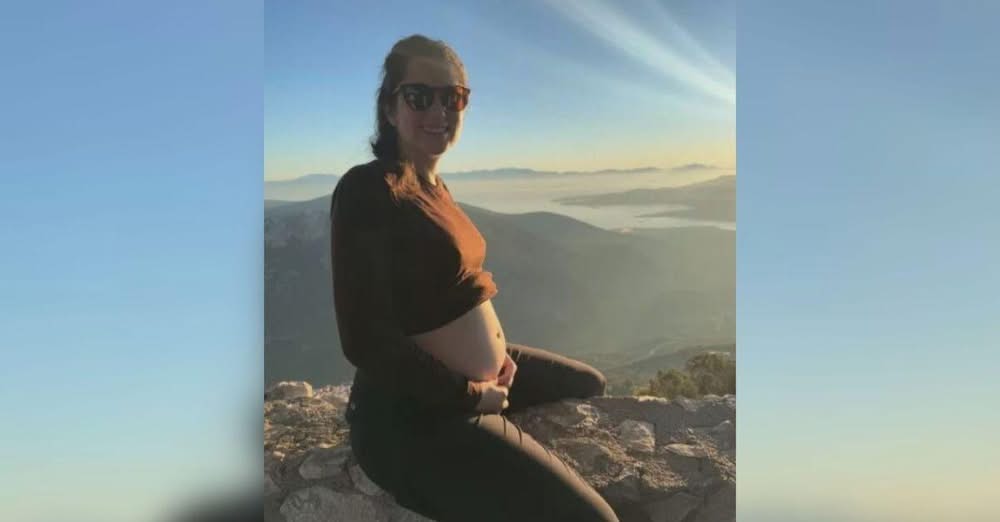 Щастливо усмихната с ръце върху корема си Зад нея слънцето